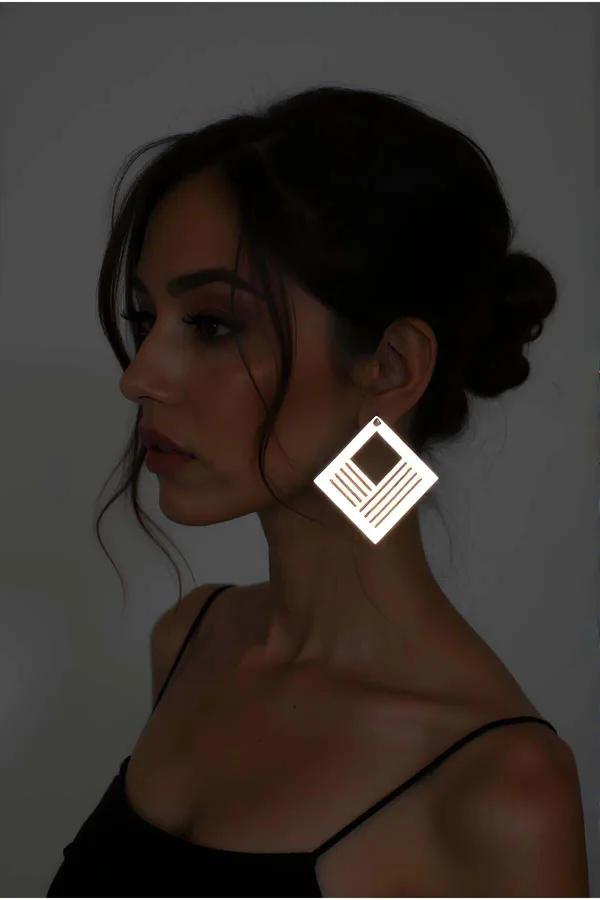 Beyaz reflektörlü geometrik kare küpe lazer kesim paralel çizgi ve merkezi kare desen, karanlık fon