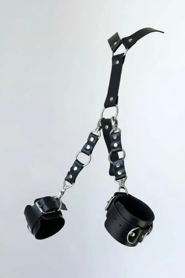 Black faux leather handcuff set with Y-strap connector, silver O-rings, swivel clasps and buckle cuffs on white background