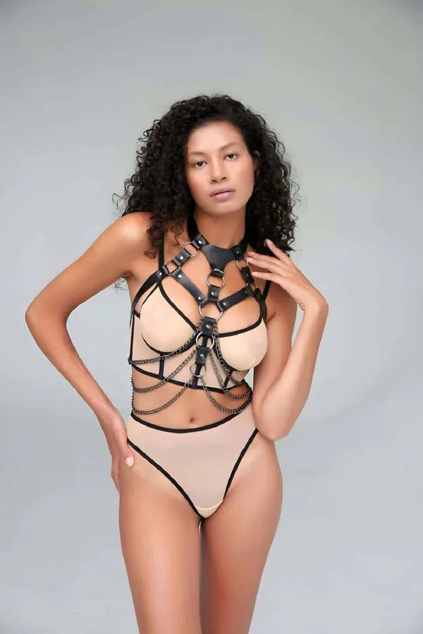 Black faux leather chest harness with cascading silver chains and four O-rings worn over nude bodysuit