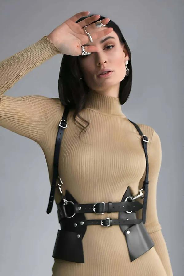 Black faux leather sculpted body harness with wide waist panels and silver buckles worn over camel ribbed turtleneck