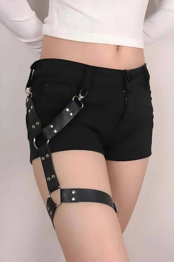 black faux leather single leg harness with silver O-rings and rivet studs worn over black shorts, hip-to-thigh adjustable str