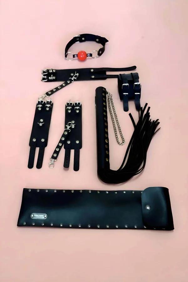 black faux leather 5-piece restraint accessory set with studded wrist cuffs red ball gag flogger whip and storage pouch on pi