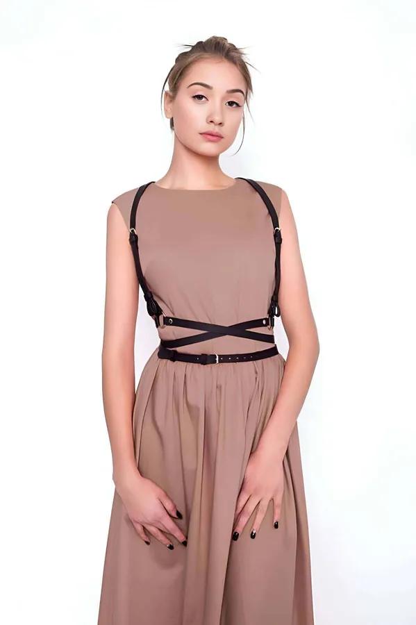 Black faux leather strappy chest harness with crisscross waist belt and gold buckles worn over a beige dress