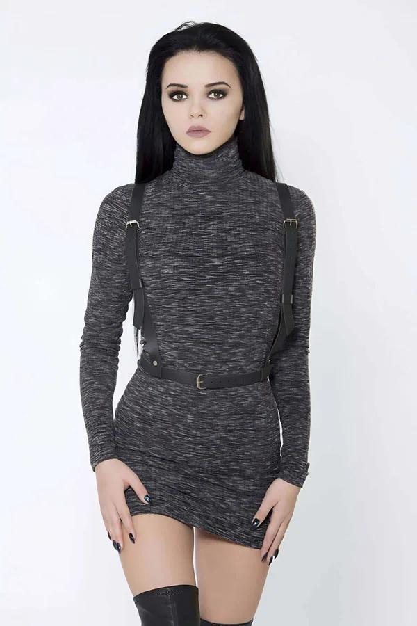 Black faux leather body harness with gold-tone buckles worn over a turtleneck dress, suspender-style shoulder straps