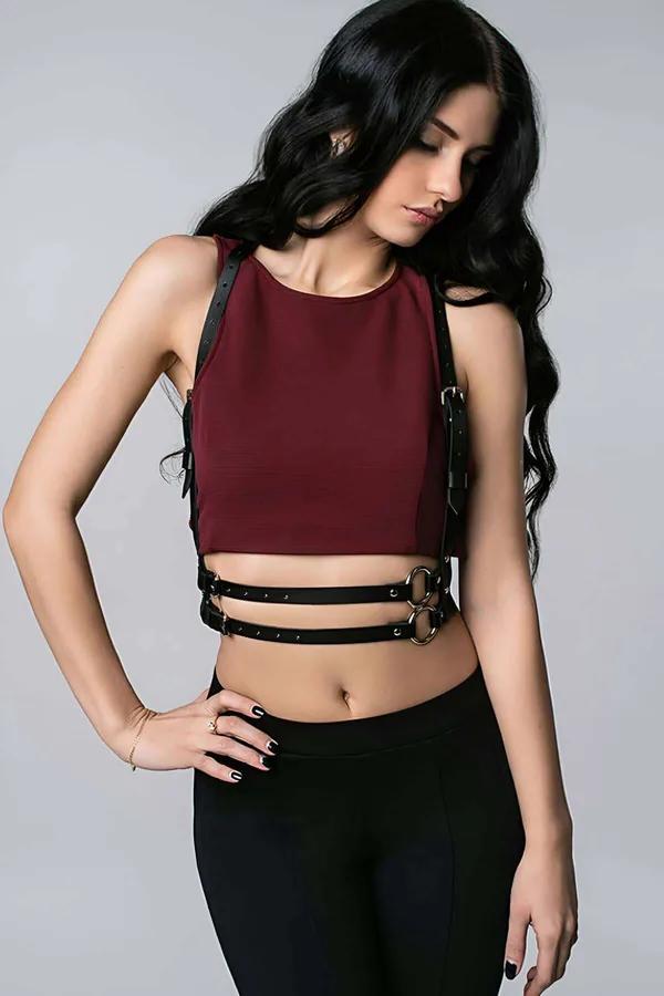 Black faux leather chest harness accessory over burgundy crop top with gold O-ring buckle detail
