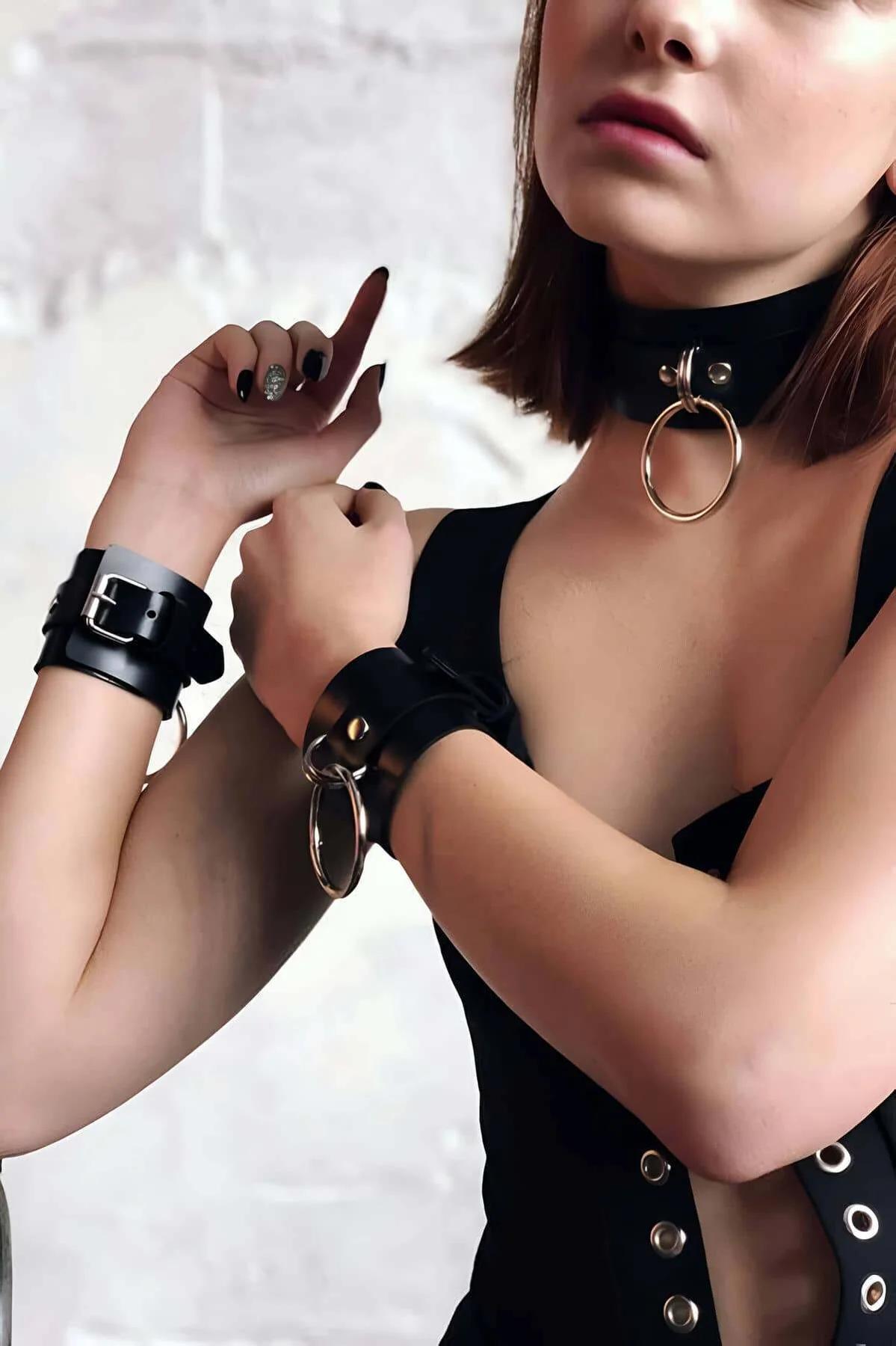 Black faux leather choker collar and wrist cuffs set with gold O-rings and adjustable buckle closures