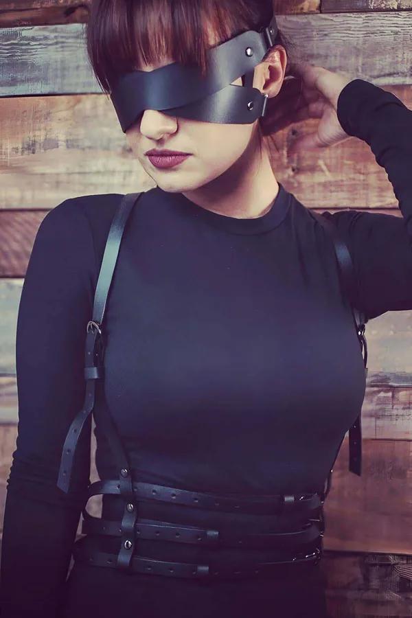 Black faux leather caged body harness with three-band waist straps and matching black blindfold mask worn over fitted clothin