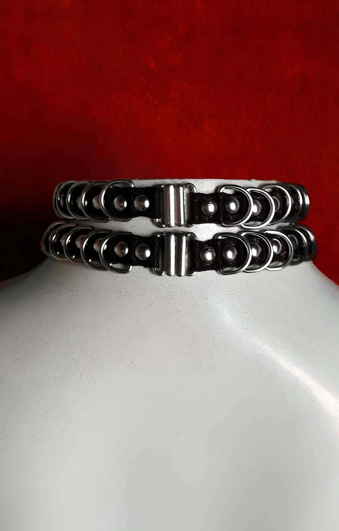Close-up of black faux leather choker band showing two rows of silver-tone interlocked rings with dome-head rivets