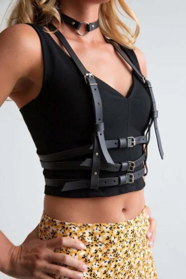Black faux leather body harness with three silver buckles at center front and matching O-ring choker worn over black crop top