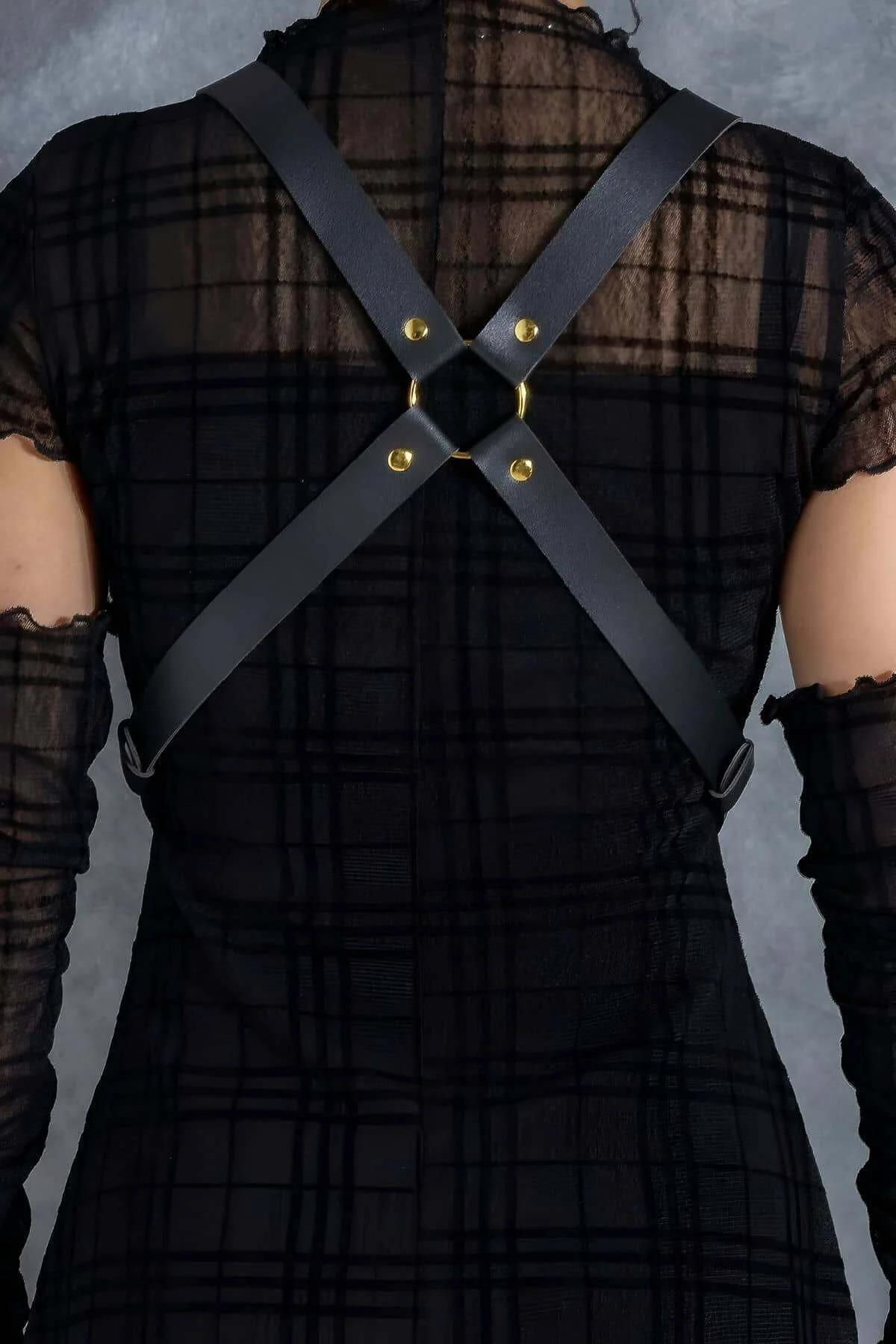 Close-up of paired gold interlocking O-rings on black faux leather chest straps with gold rivet detail