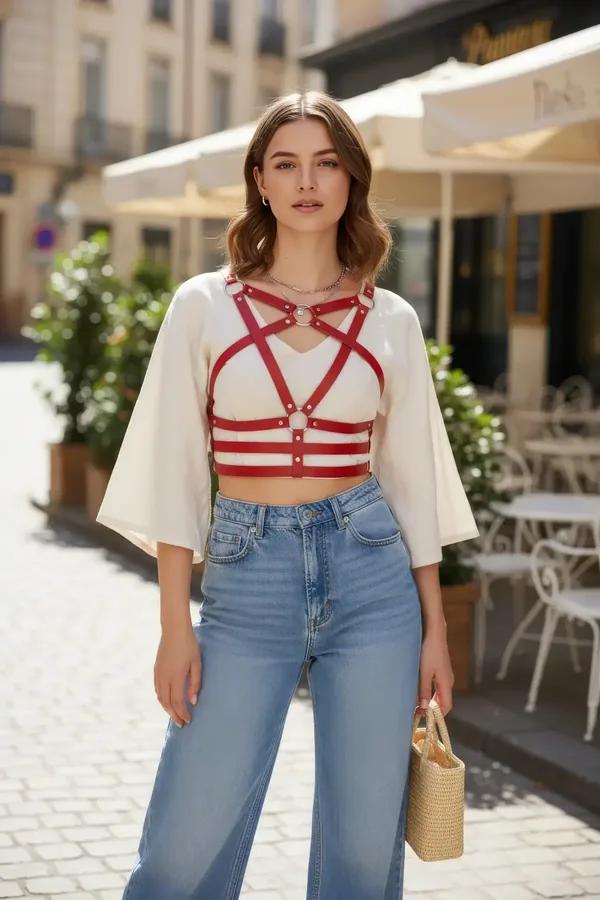 Red faux leather caged chest harness with three silver O-rings worn over white crop top and jeans