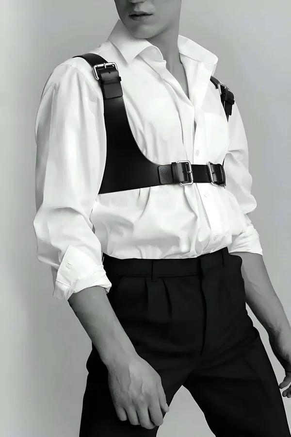 Black faux leather chest harness vest with wide shoulder straps and dual silver buckles worn over white shirt