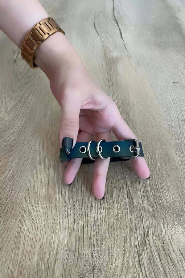 Iridescent teal faux leather finger harness with two silver O-rings and pin buckle worn across hand fingers