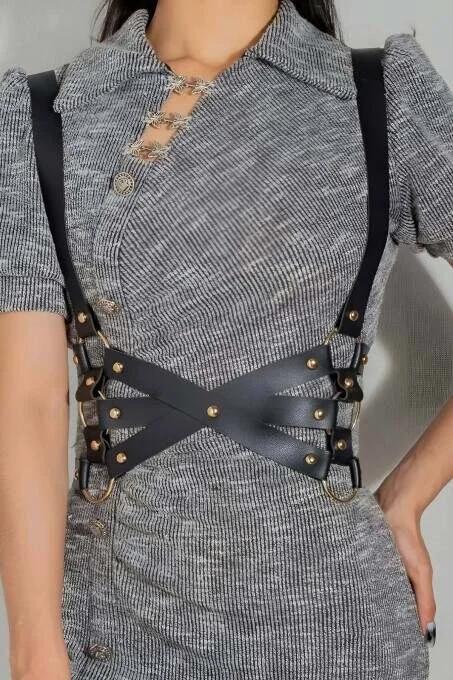 black faux leather cross-back body harness with gold dome studs and O-rings worn over gray knit dress