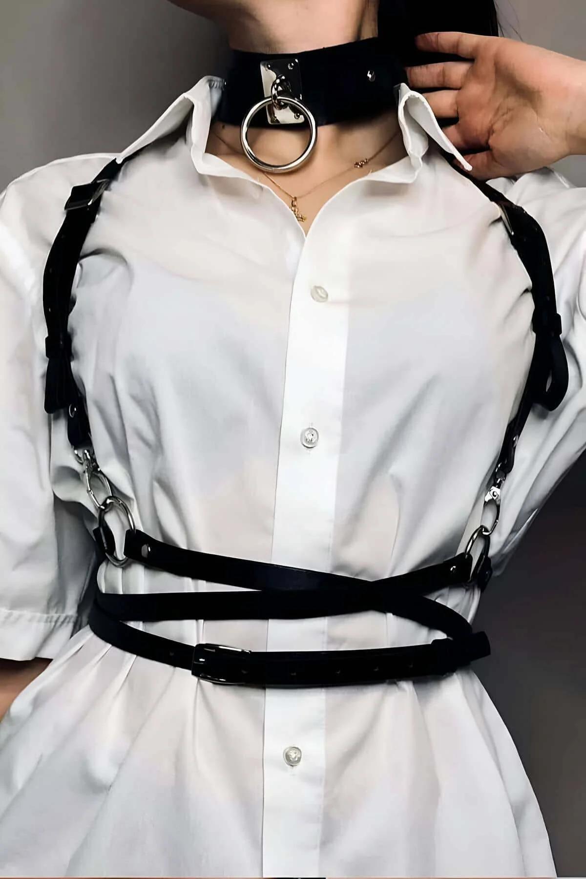 Black faux leather chest harness with silver O-ring choker worn over white button-down shirt, showing diagonal shoulder strap