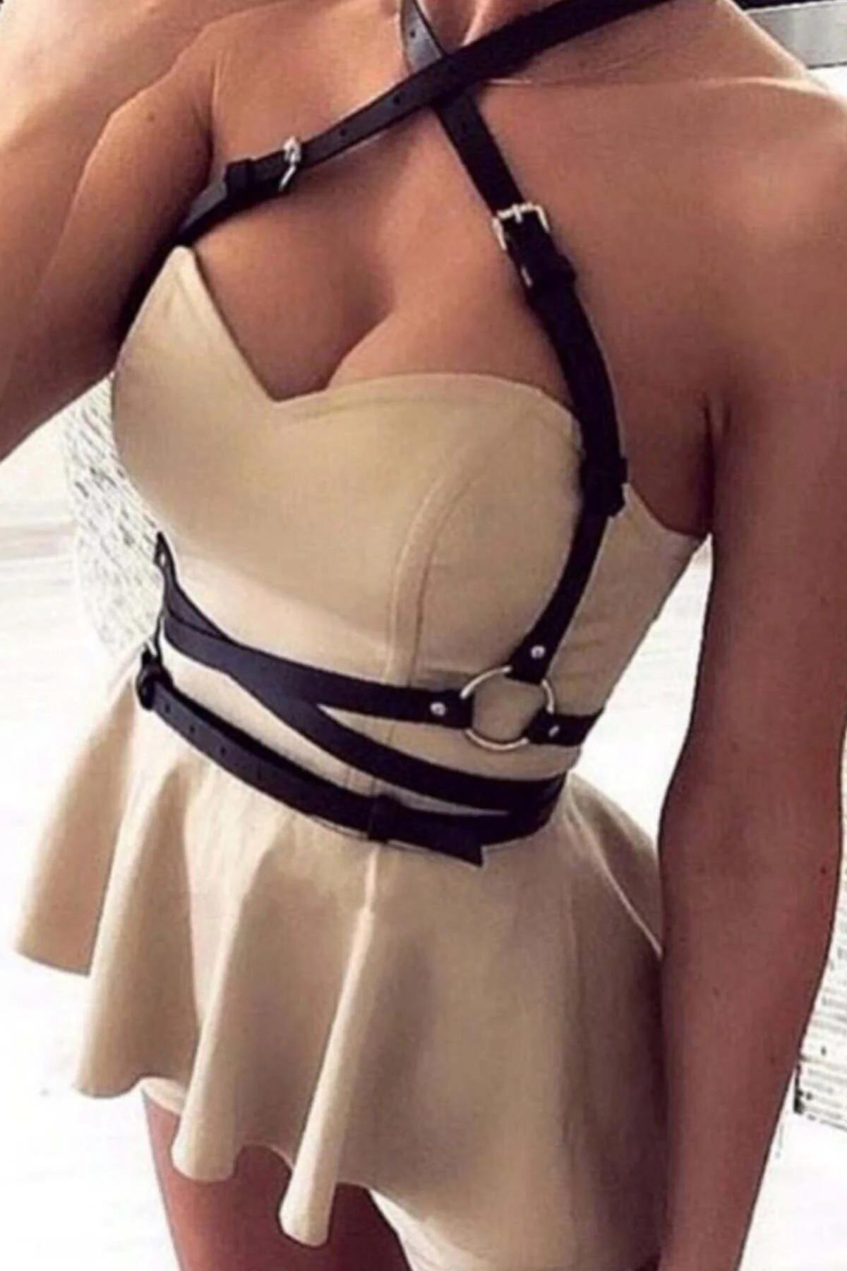 Black faux leather caged body harness with silver O-ring at waist, worn over cream strapless dress