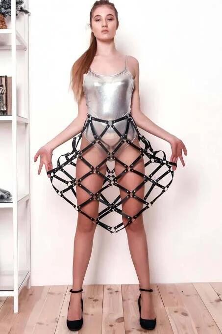 Black faux leather grid cage skirt harness with gold stud rivets and adjustable thigh straps worn over silver bodysuit